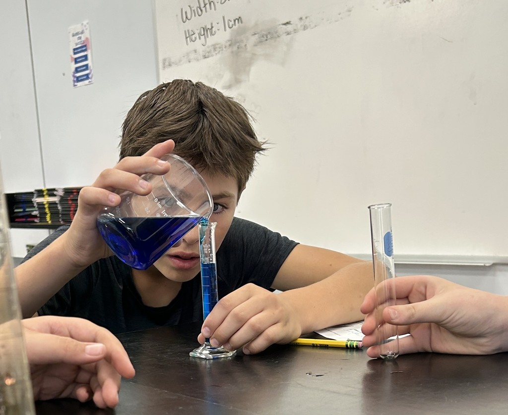 A student pours liquid from a beaker into a graduated cylinder. 