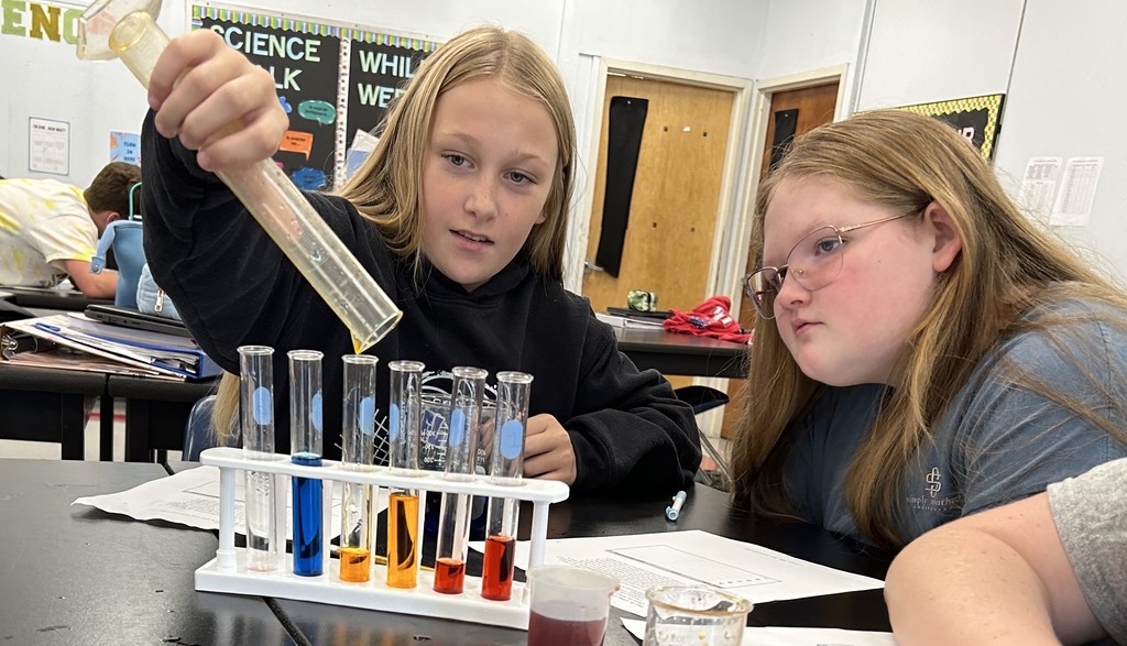 A student pours liquid from a beaker into a graduated cylinder. 