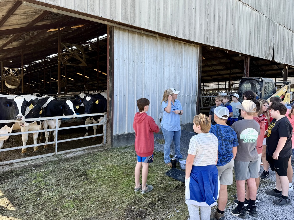 Students listen to a farmer beside a cattle barn.