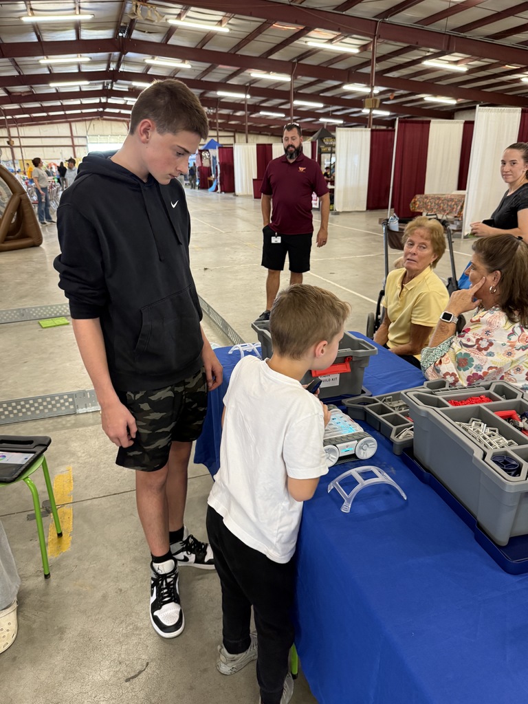 An older student helps a younger student work on a robot.