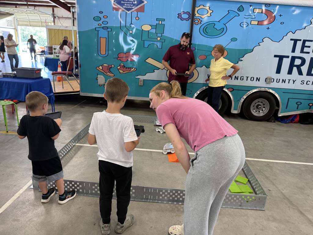 An older student helps a younger student work on a robot.