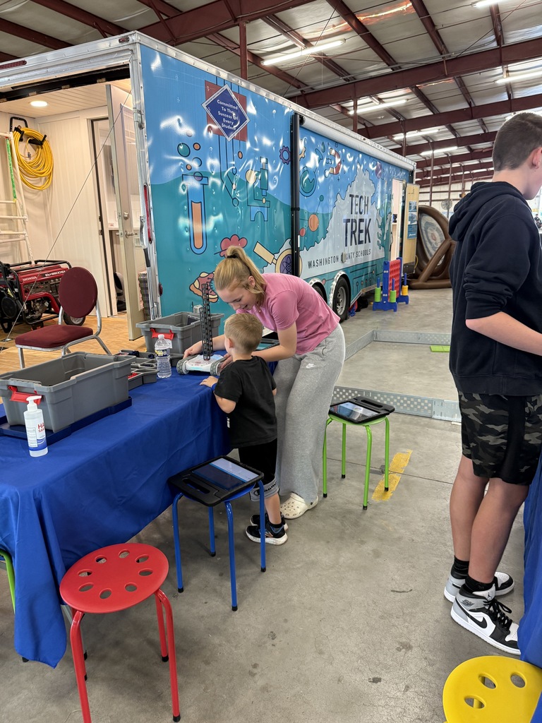 An older student helps a younger student work on a robot.