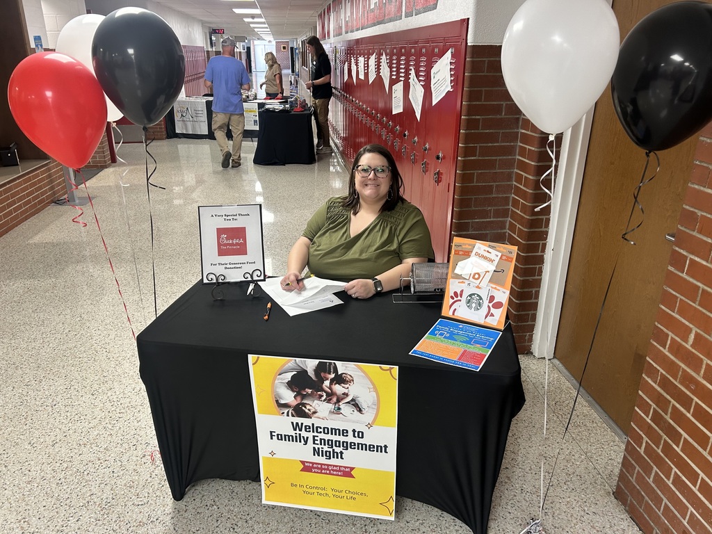 A woman sits at a welcome table in a school hall.