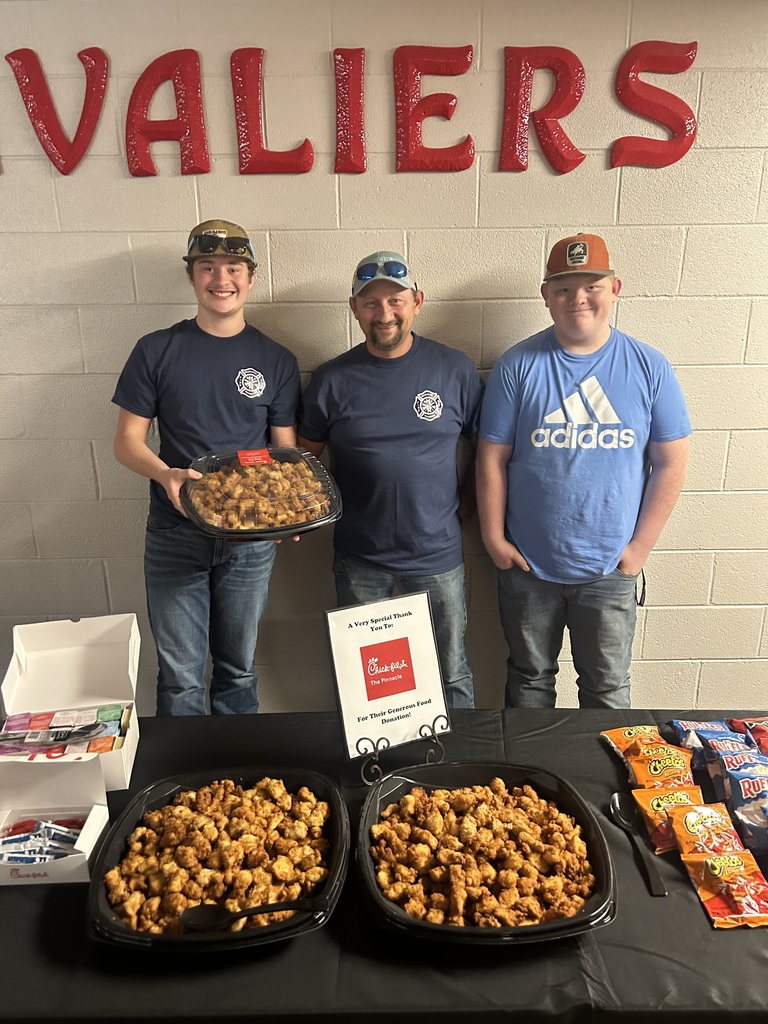 Three men stand with chicken at a table in a cafeteria.