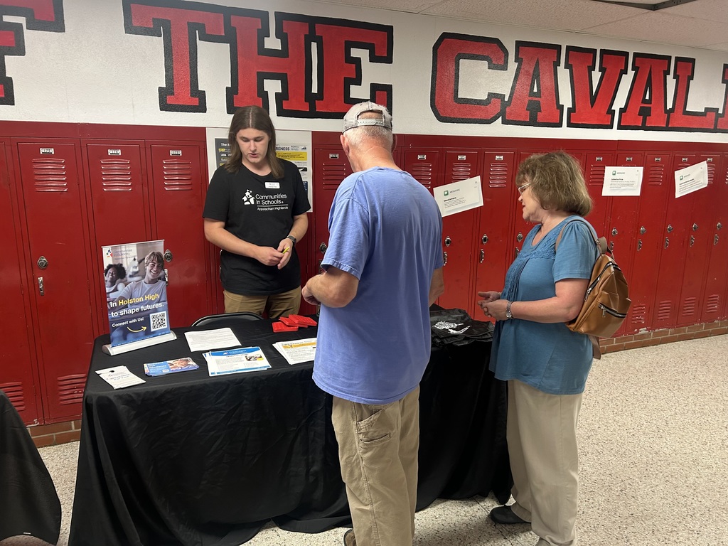 A man talks to two parents at an informational table.