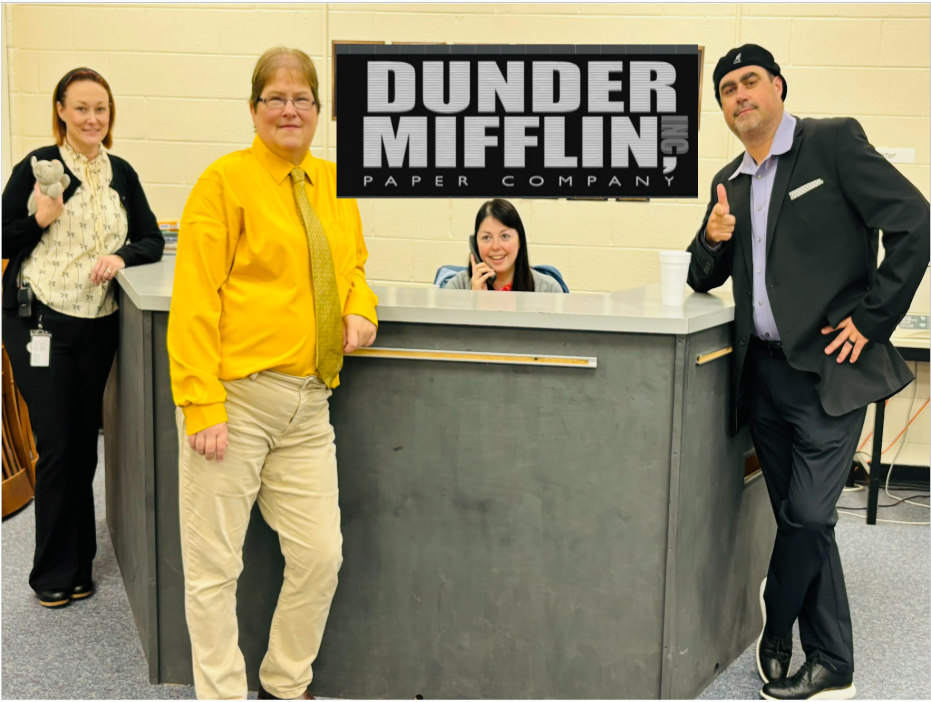The office staff in costume poses in a library.