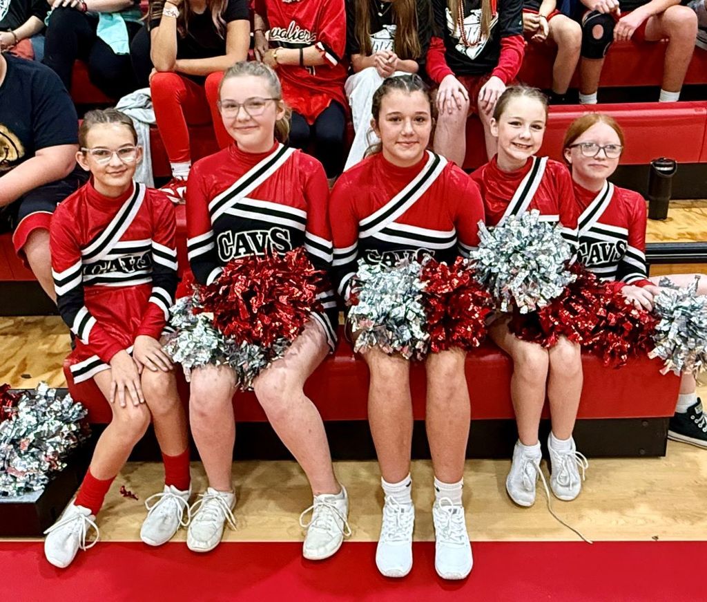 Cheerleaders sit in a gym.