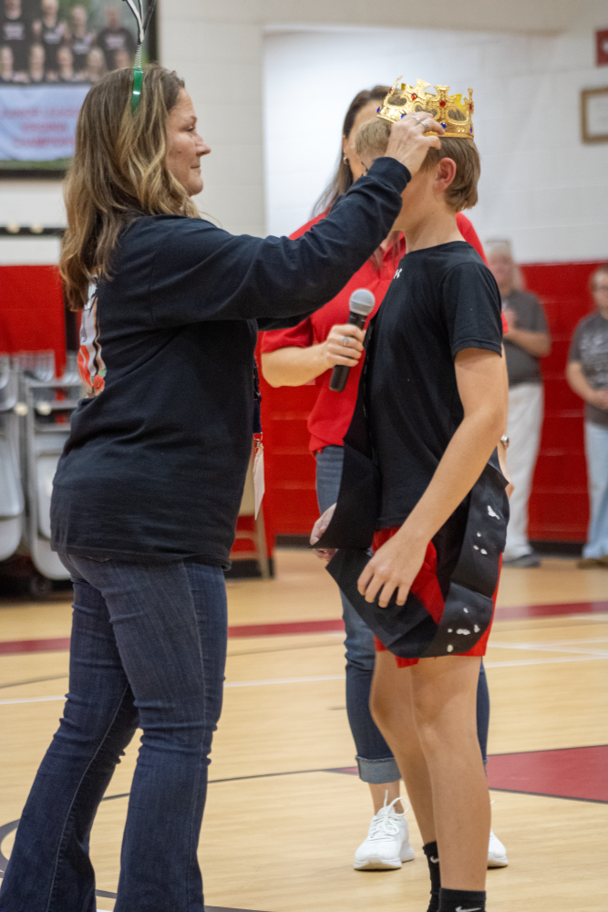 A teacher crowns a student in a gym.