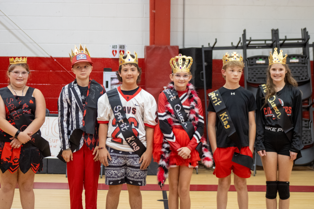 Students wearing crowns pose in a gym.