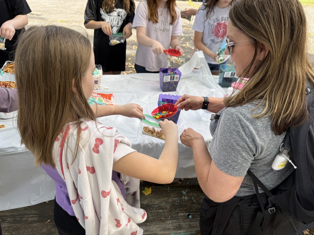A woman puts candy in a student's bag of trail mix.