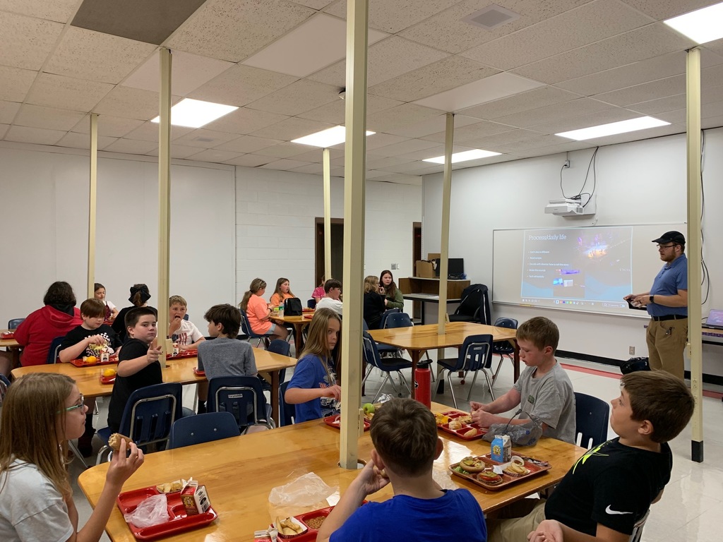 Students eat lunch while a man talks with them.