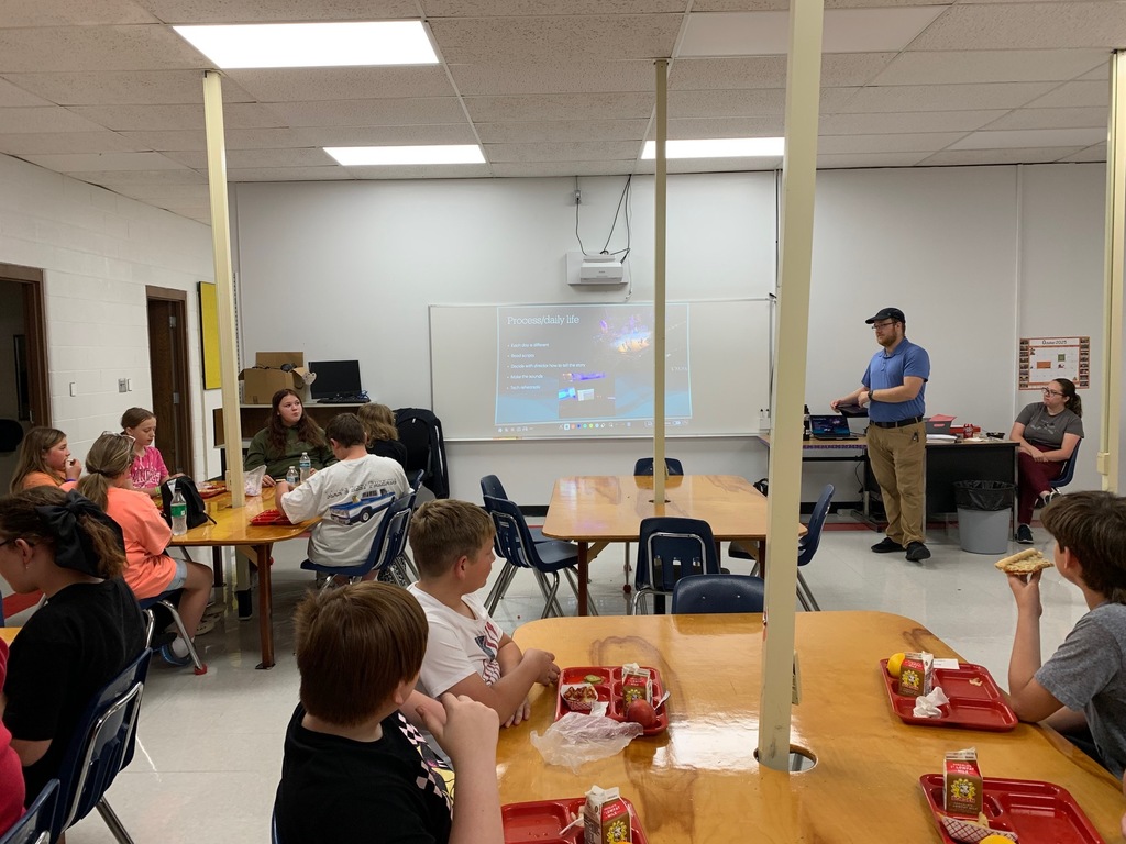 Students eat lunch while a man talks with them.