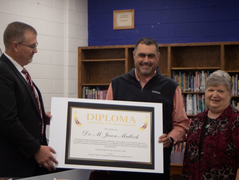 Three people hold a diploma in a library.