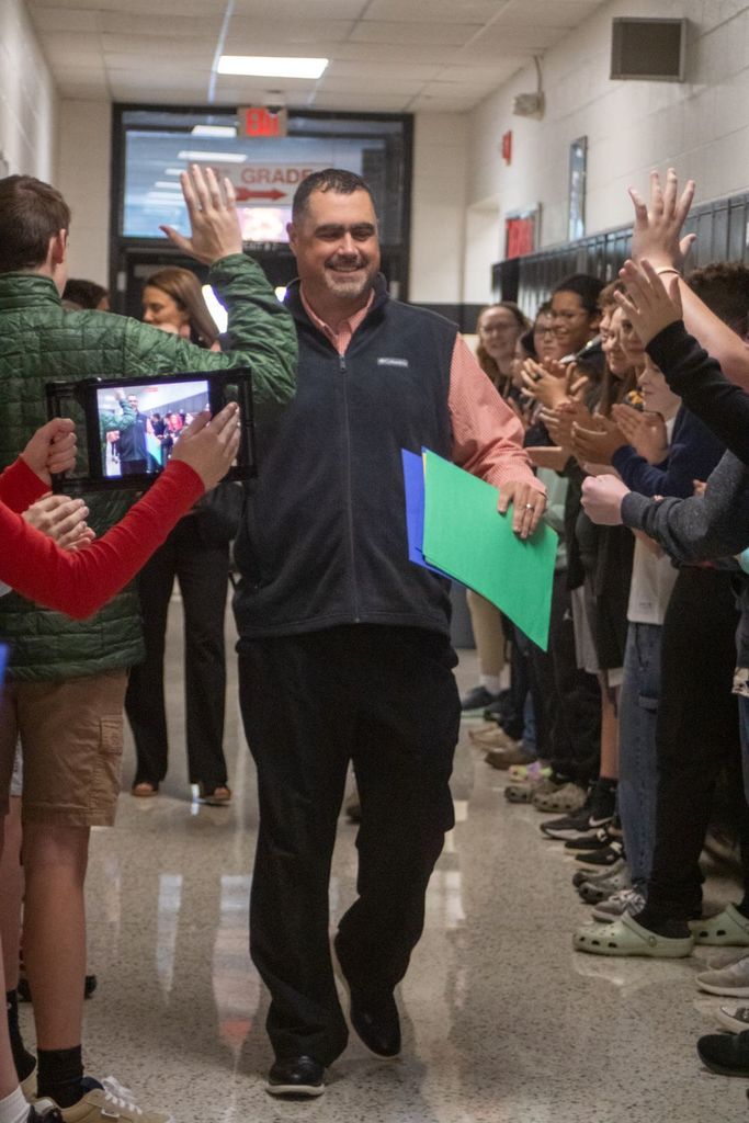A man walks down a hall of children clapping.