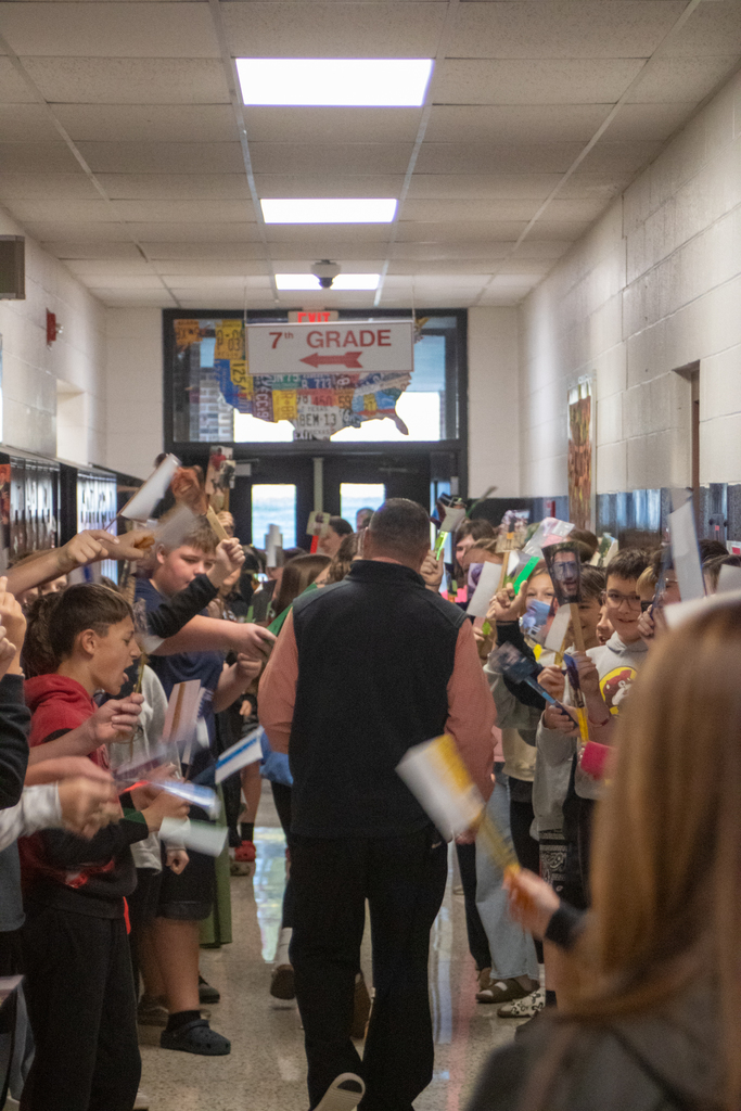 A man walks down a hall lined with children holding pictures.