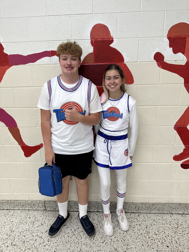 Two students dressed in basketball jerseys pose in a cafeteria.