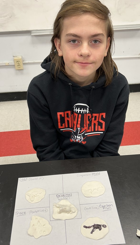 A student holds fossils made with clay and plastic dinosaurs.