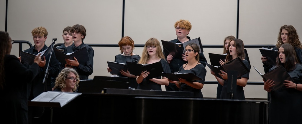 Students sing on risers on a stage.