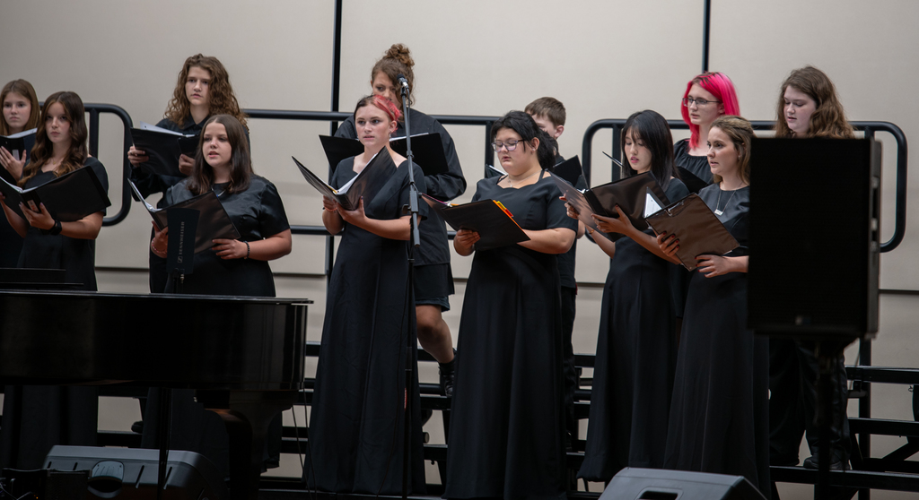 Students sing on risers on a stage.
