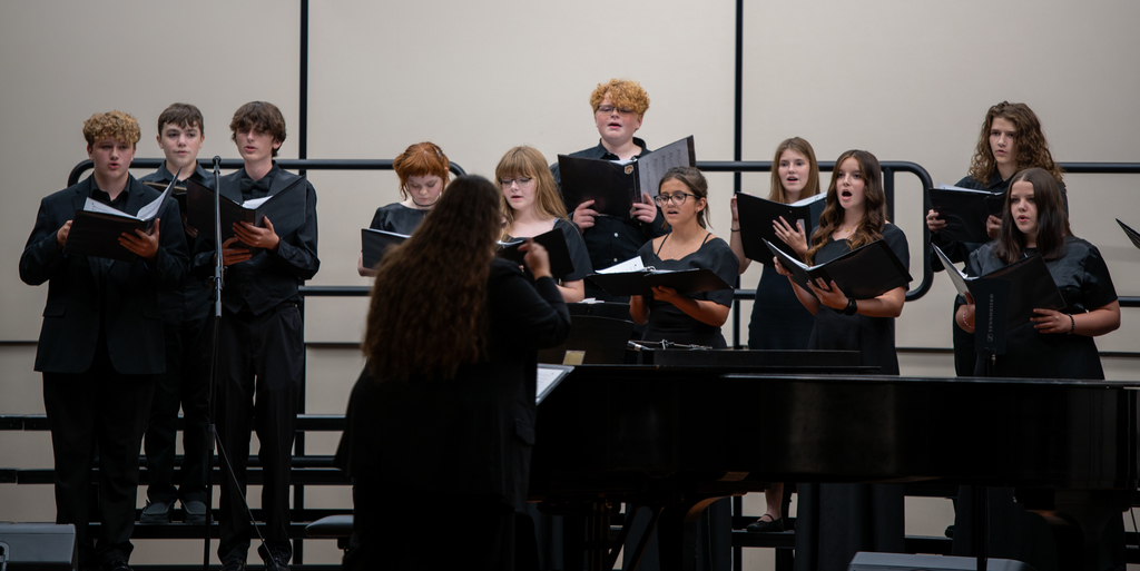 Students sing on risers on a stage.