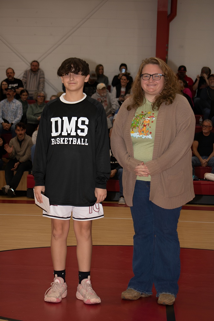 A teacher stands with a student athlete in a gym.