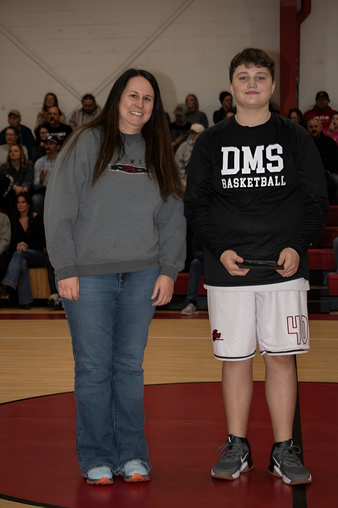 A teacher stands with a student athlete in a gym.