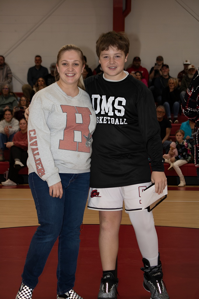 A teacher stands with a student athlete in a gym.