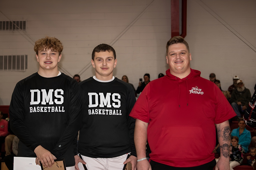 A teacher stands with student athletes in a gym.