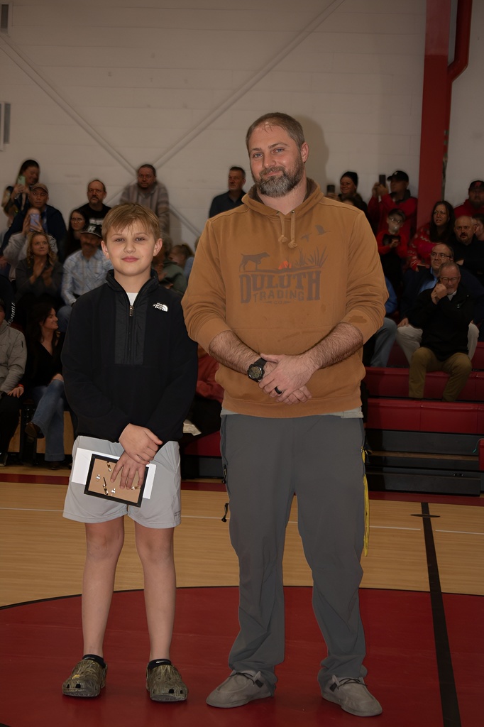 A teacher stands with a student athlete in a gym.