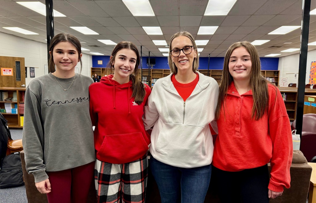 A teacher stands with student athletes in a library.