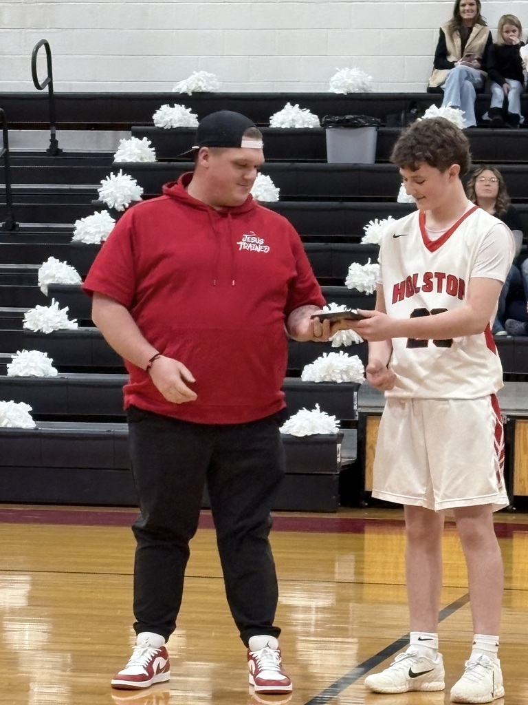 A teacher stands with a basketball player in a gym. 