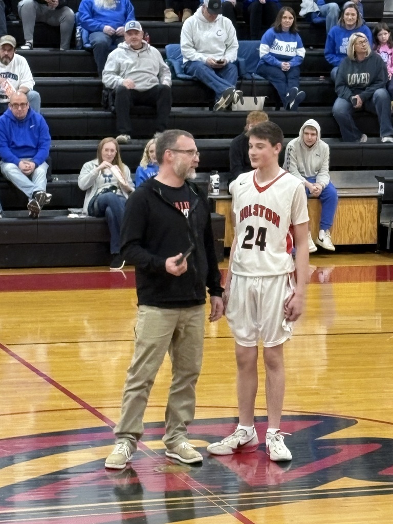 A teacher stands with a basketball player in a gym. 