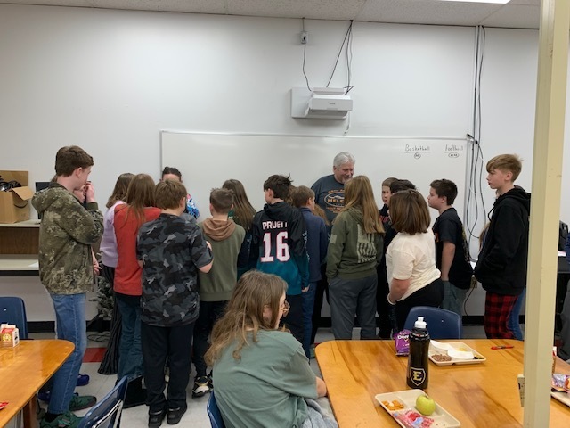 Students talk to a man in a classroom.