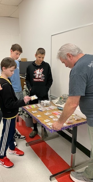 A man shows students fishing bait in a classroom.