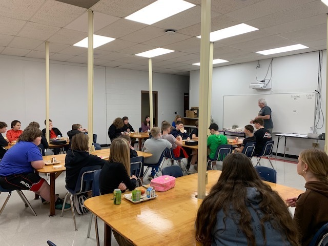 Students listen to a man talk in a classroom.