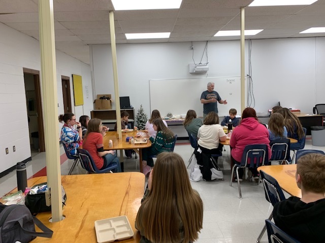 Students listen to a man talk in a classroom.