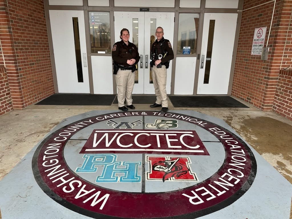 Two school resource officers stand in front of a school.
