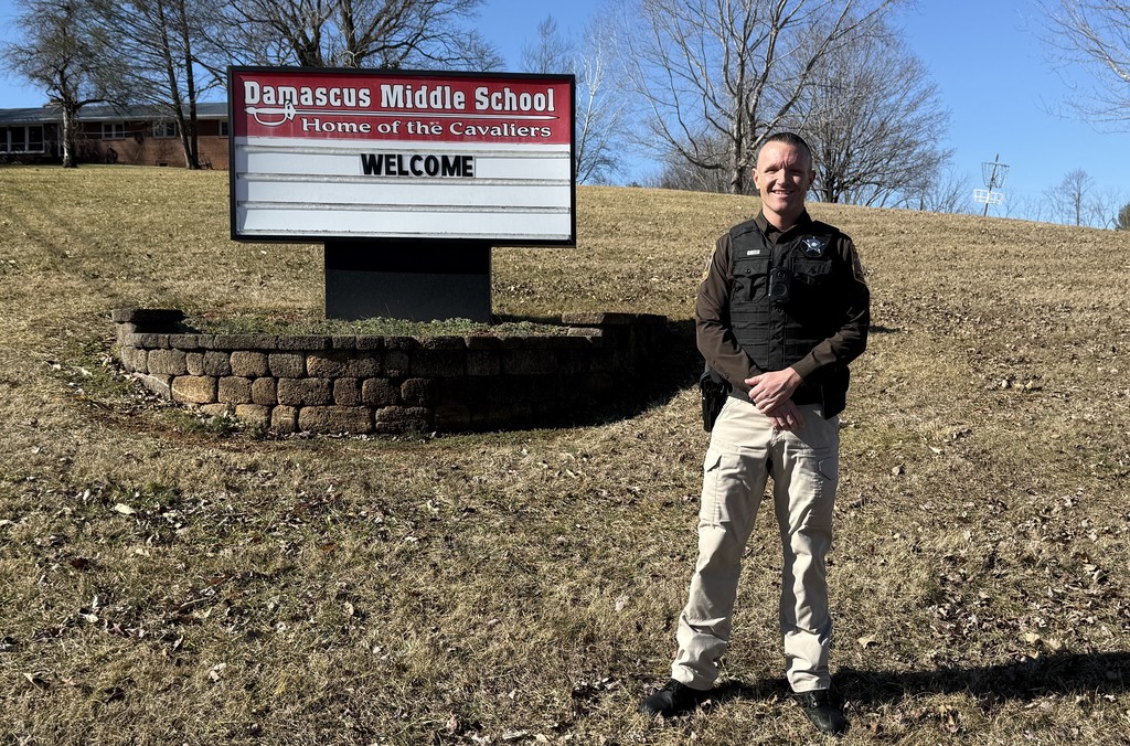 A school resource officer stands in front of a Damascus Middle School sign.