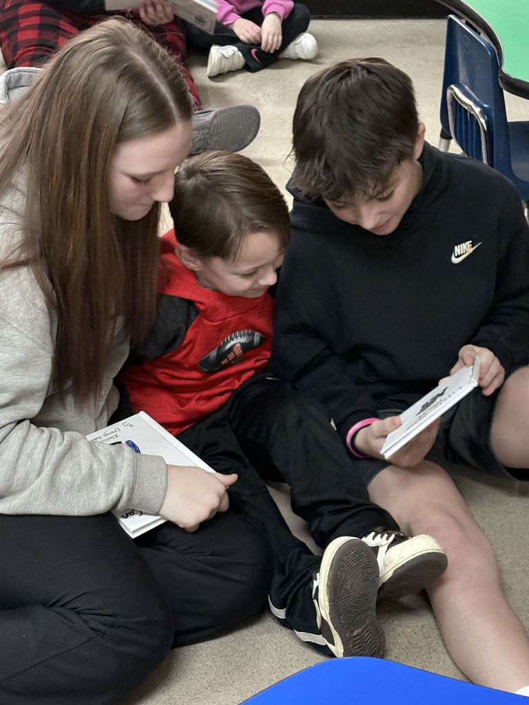Two older students read to a younger student.