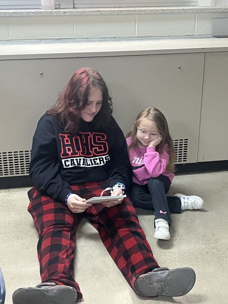 An older student reads to a younger student.