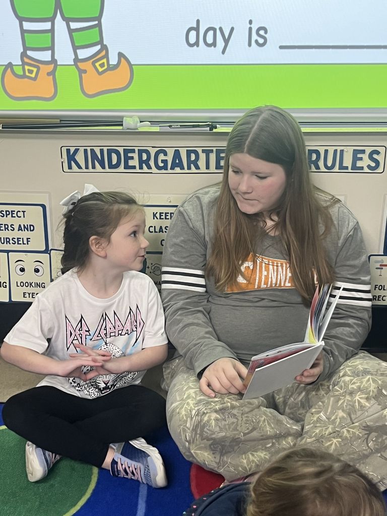 An older student reads to a younger student.
