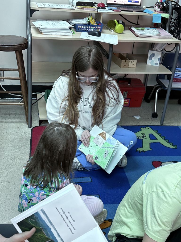 An older student reads to a younger student.