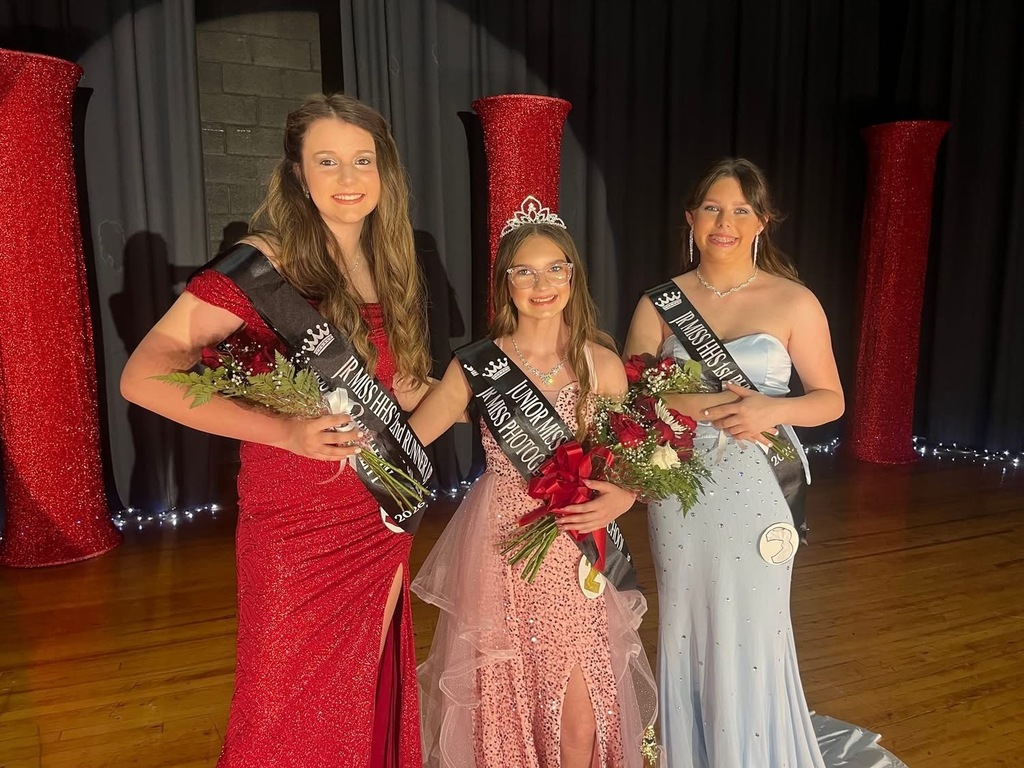Three middle school girls wearing pageant dresses pose on a stage.