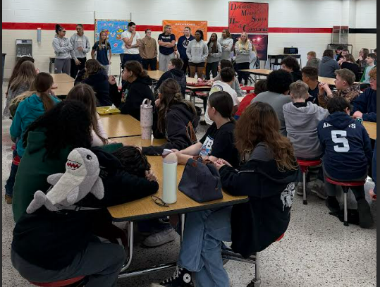 College basketball players talk with younger students in a cafeteria.