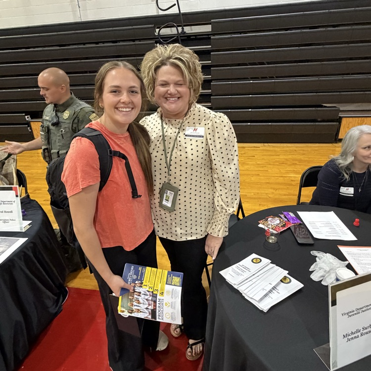 A woman stands with a student in a gym.