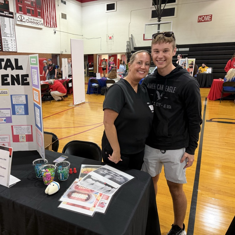 A woman stands with a student in a gym.