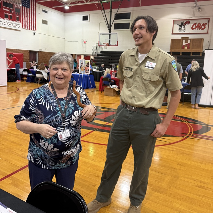A woman poses with a wildlife officer and a snake in a gym.