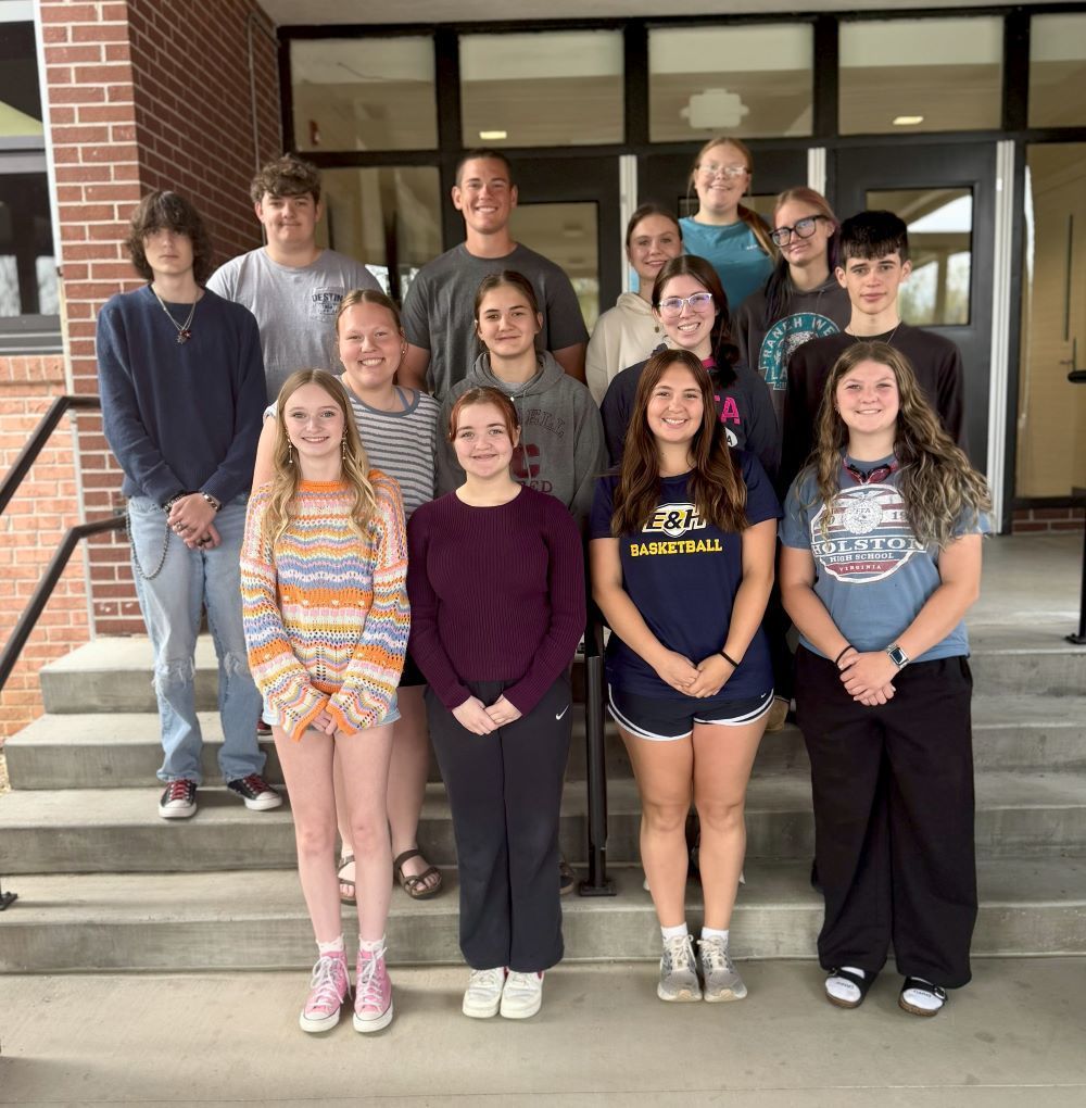 A group of students pose on stairs at the entrance of a school.