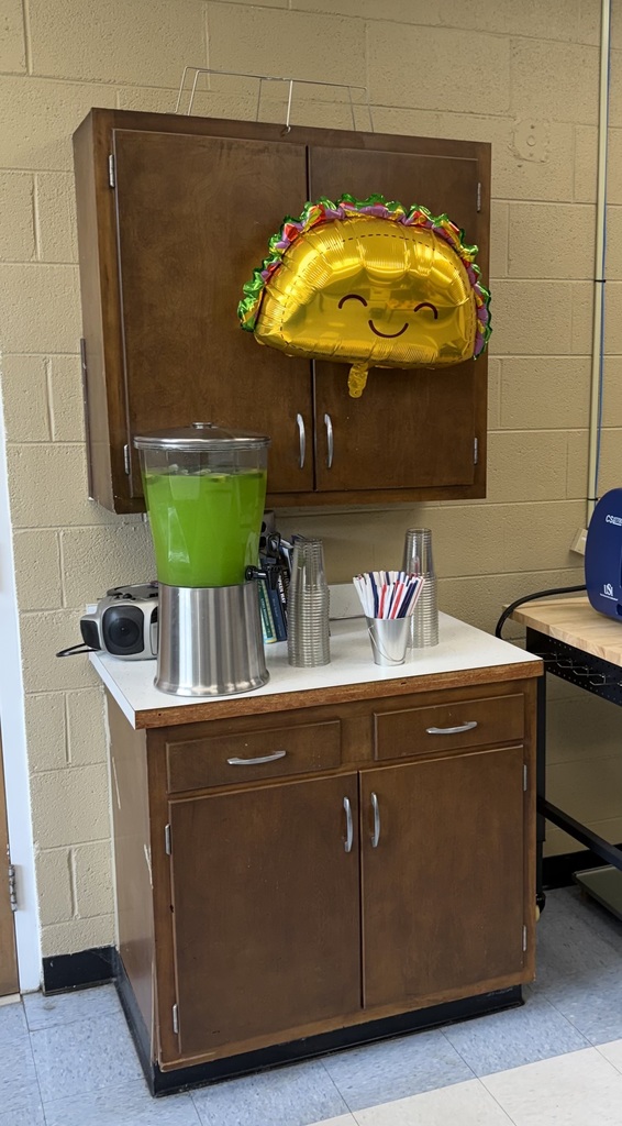 A container of green lemonade on a counter with a taco balloon over it.