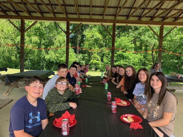 Students eat lunch at a table in a picnic shelter.